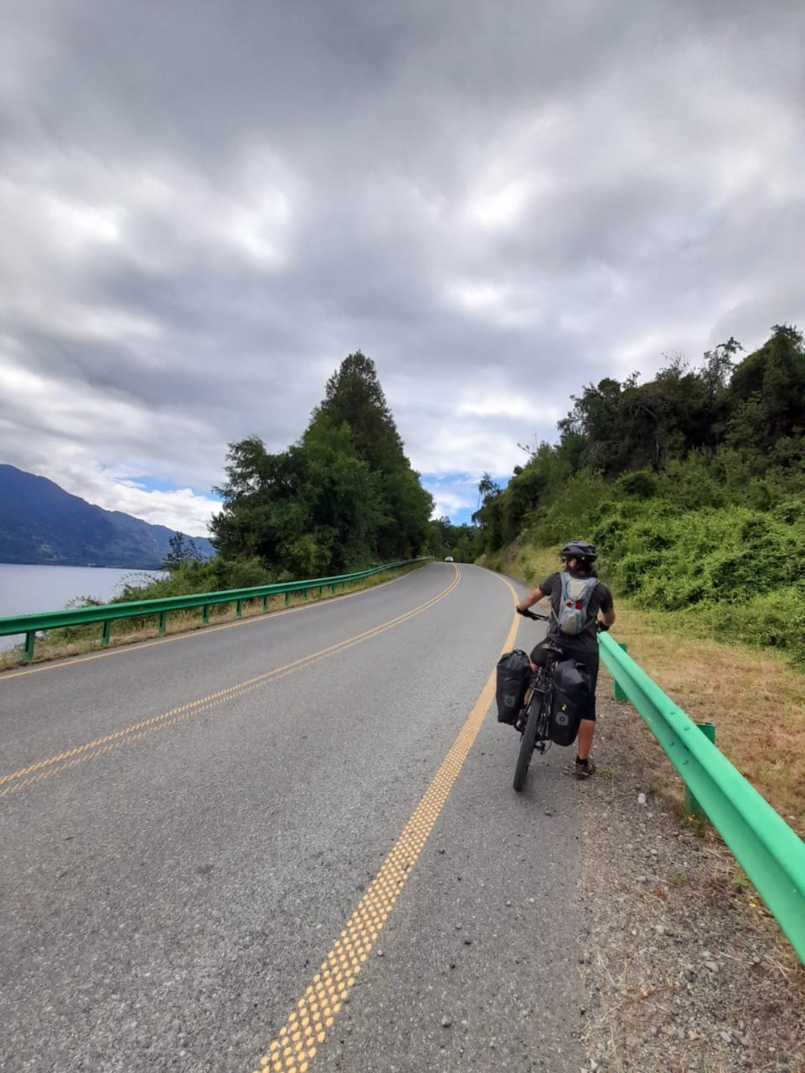 Ciclista con alforjas junto al lago y baranda verde